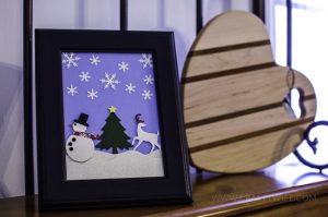Use paper crafts to create a winter wonderland picture display for your home. Use a snowman hole punch and other paper craft items to create the scene.