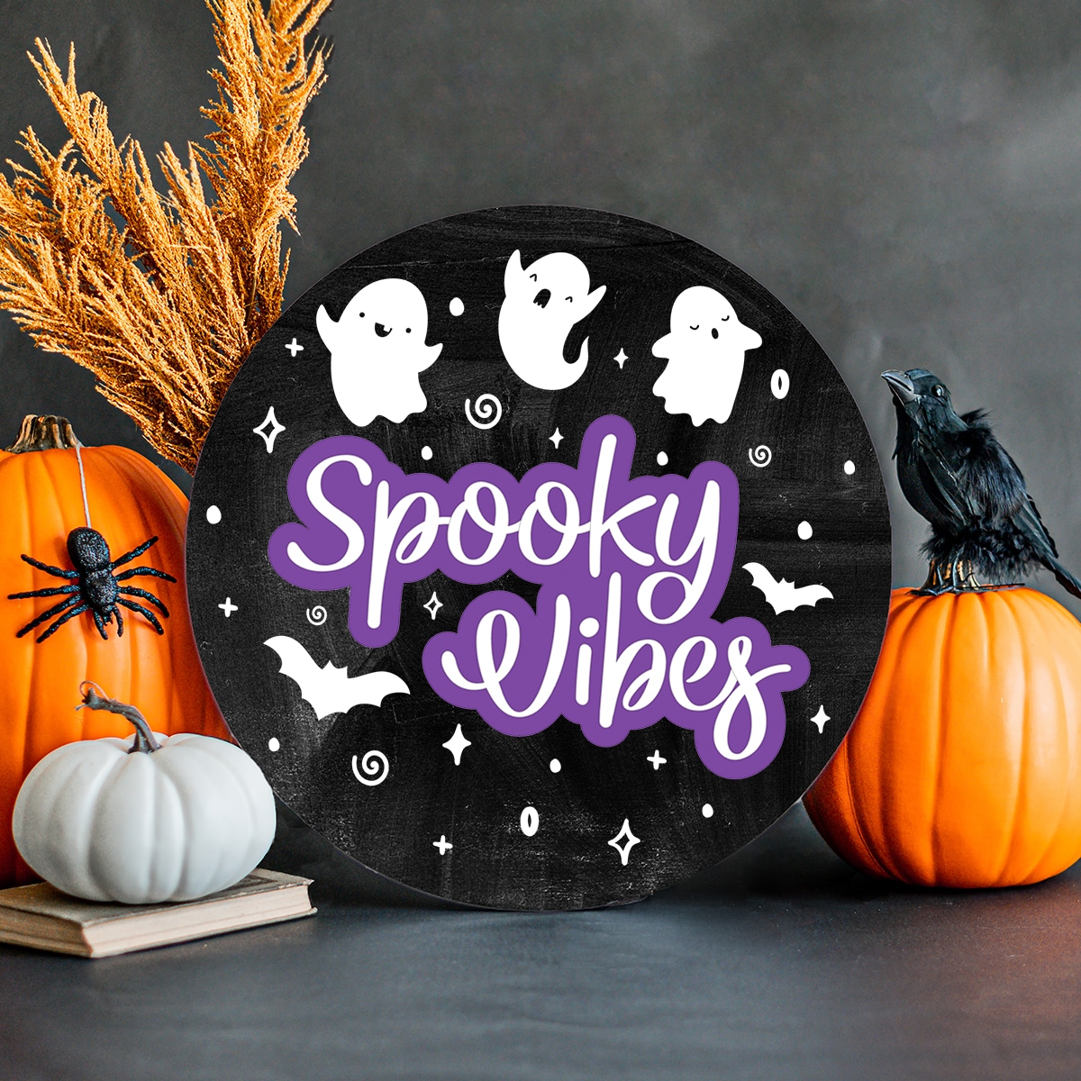 black wood round with three white ghosts at the top and the words spooky vibes underneath.