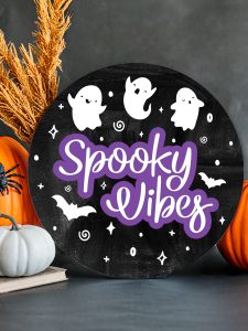 black wood round with three white ghosts at the top and the words spooky vibes underneath.